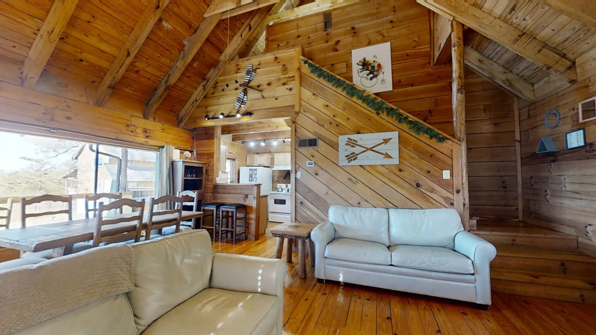 The spacious and welcoming living and dining area is framed by exposed wooden beams and filled with comfortable seating. The inviting atmosphere is enhanced by a cozy fireplace, decorative wall art, and a large window that offers scenic views. This space is clearly designed for families to gather, share meals, and unwind after eventful days exploring nearby attractions.