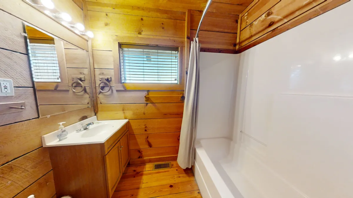A tranquil bathroom scene featuring a sleek bathtub beneath a window with blinds, wooden paneling, and a sink with a modern faucet. The scene suggests a soothing, spa-like space perfect for unwinding after an active day.