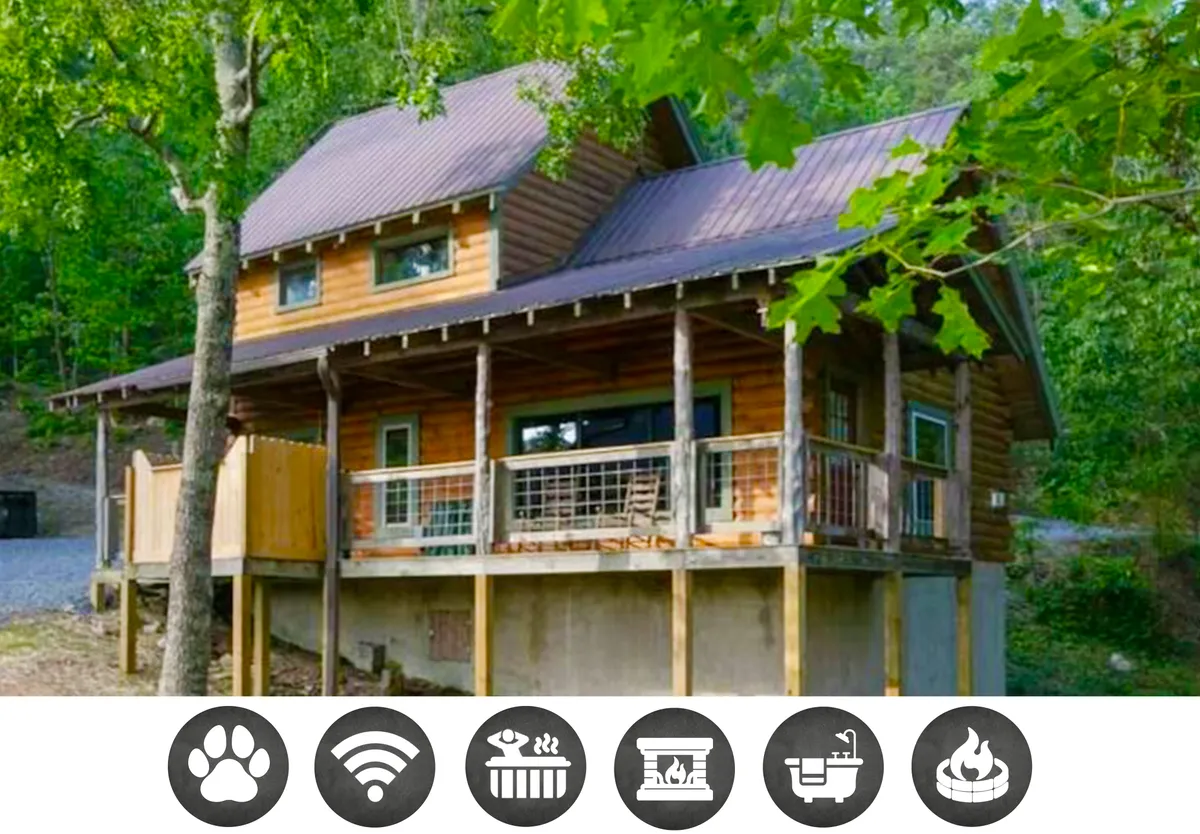 The image showcases the charming log cabin exterior of Adelaide's Den, nestled among lush green trees, with a welcoming front porch perfect for relaxing while immersed in nature.