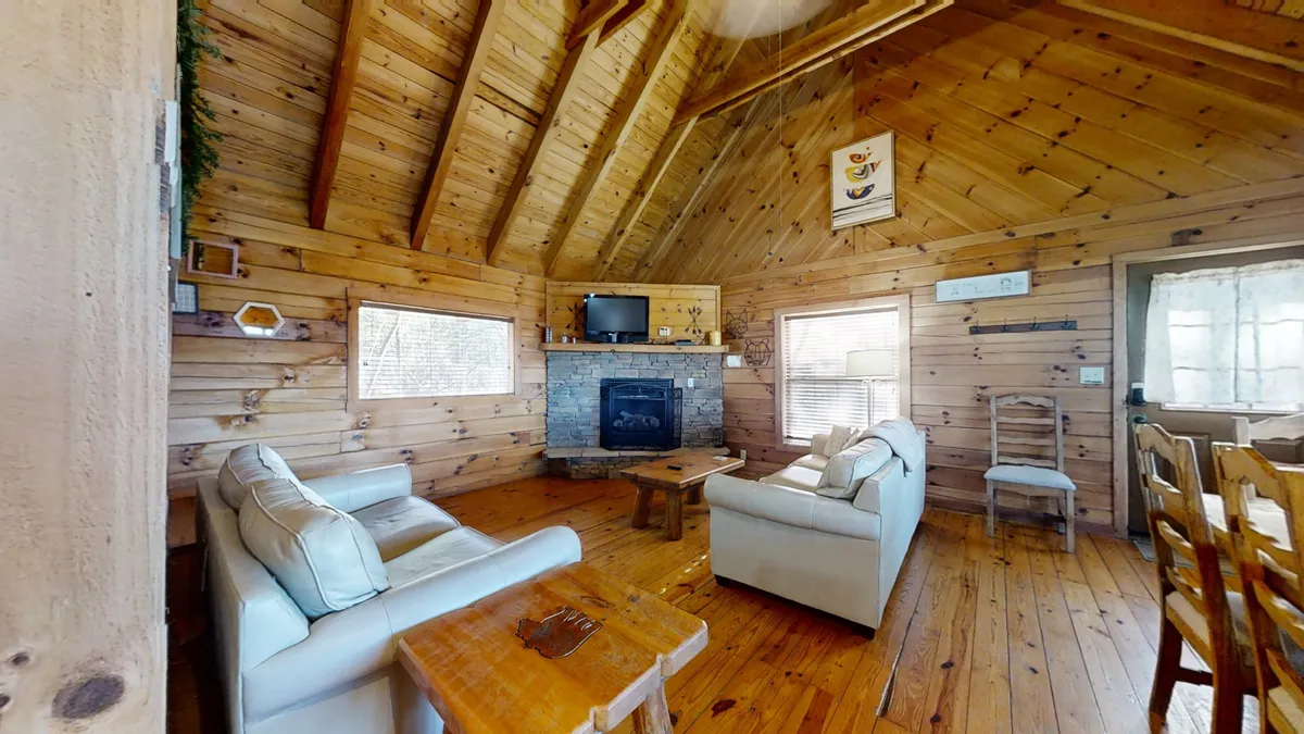 A close view of a welcoming living area featuring a glowing fireplace, a comfortable sofa, wooden floors, and exposed ceiling beams. The setup invites relaxation, socializing, and enjoying evenings by the fire, echoing the 'cozy gathering' spirit described in the content.