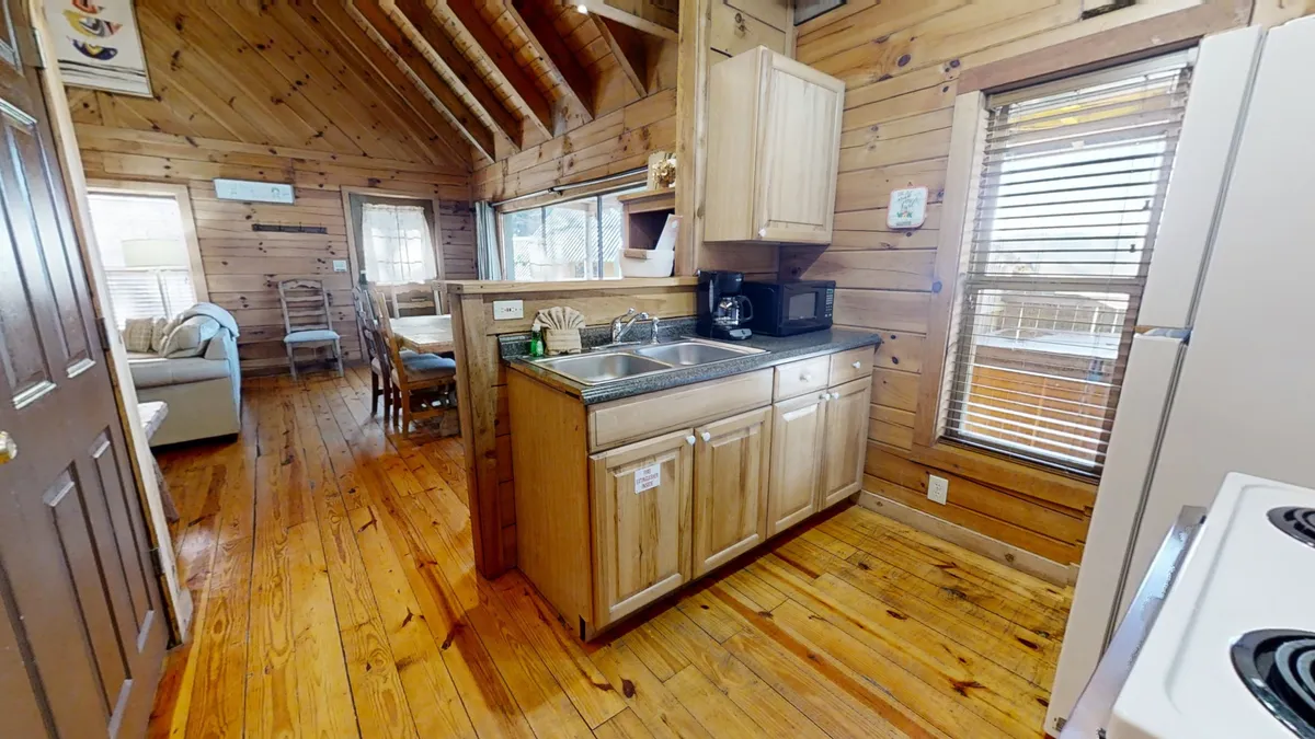 This interior view features the kitchen sink, wooden cabinetry, a visible dining area, and part of the living area seating. The open-plan design encourages interaction and togetherness, showcasing the kitchen and dining area's proximity.