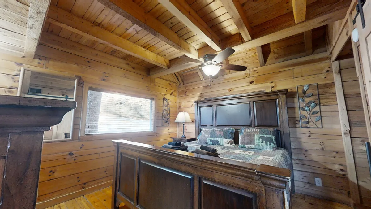 This image showcases a cozy bedroom with a comfortable bed framed by rustic wooden beams, a soft bedside lamp casting a warm glow, and a window that lets in natural light. The inviting atmosphere makes it feel like an intimate retreat, ideal for relaxing or unwinding after a mountain adventure.